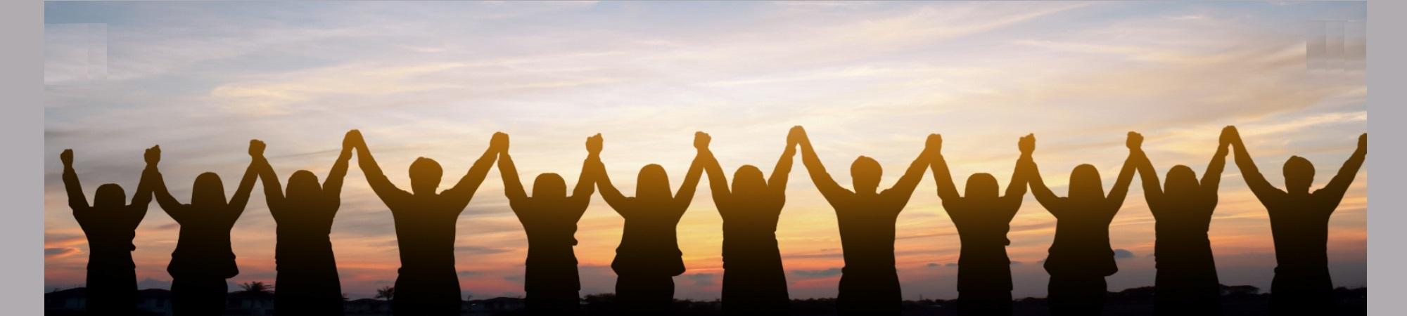 10 attendees silhouetted against a sunset. Holding hands and arms up. 