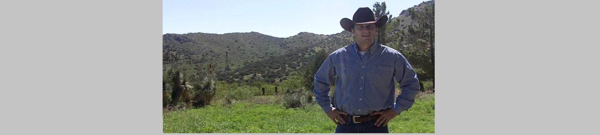 A Rancher standing in his ranch. Black cowboy hat, chambray shirt.