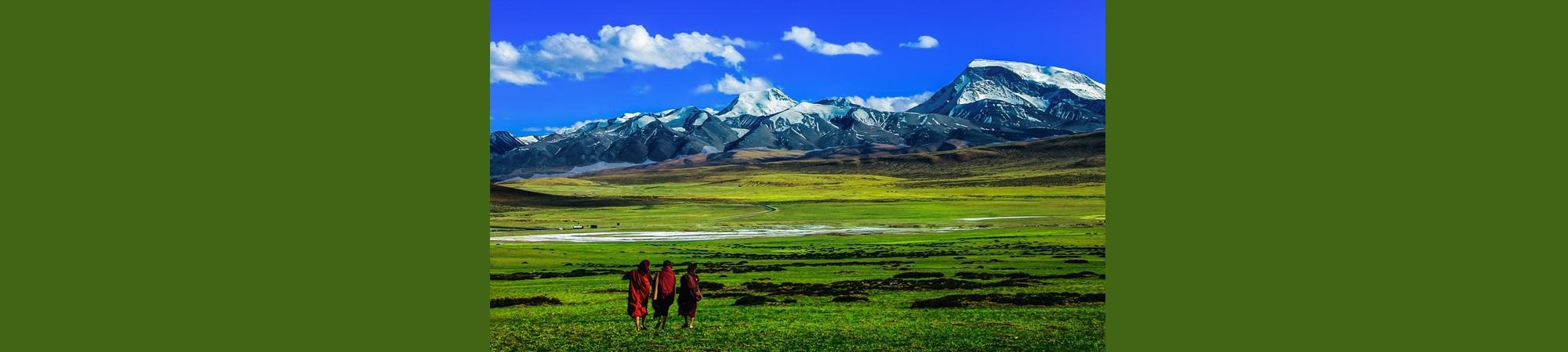 Three humans in the distance in a large grassy landscape with mountains