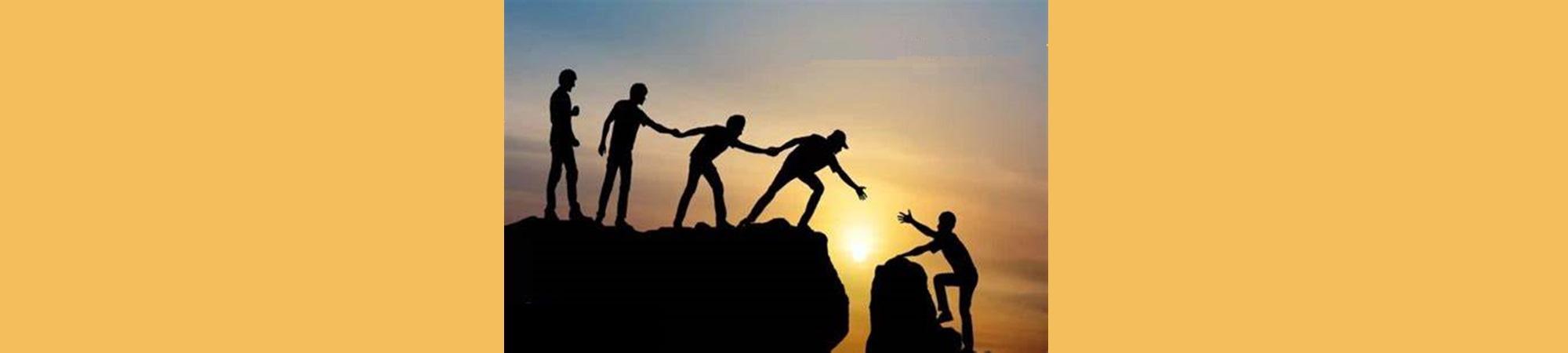 Four persons helping a fifth one climb up a rock